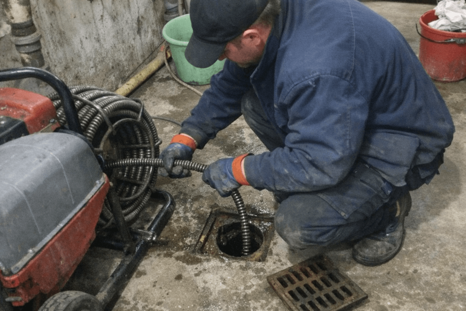 Monteur führt eine mechanische Reinigung an einem Bodenablauf in einem Kellerraum durch